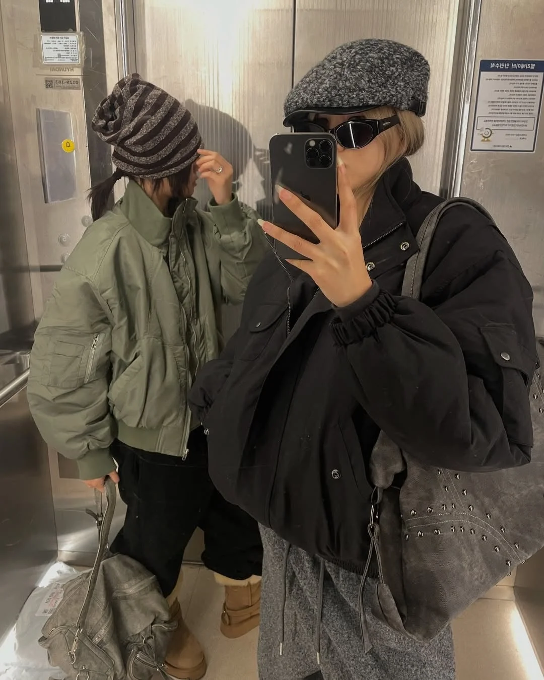 エレベーターの中で冬のカジュアルな装いをした2人の女性がセルフィーを撮っています。