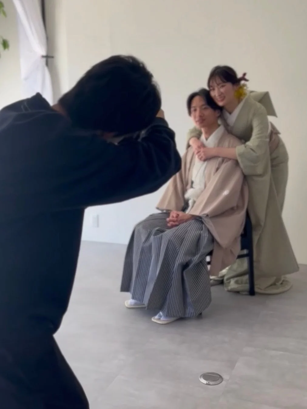 フォトスタジオで和装のカップルが笑顔でポーズをとっており、カメラマンが撮影している様子を捉えた一枚です。