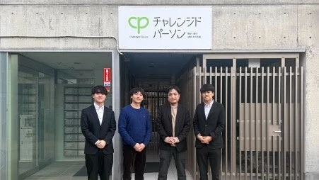 「チャレンジドパーソン」という看板が掲げられた建物の入口前で、4人の男性が並んで立っている集合写真