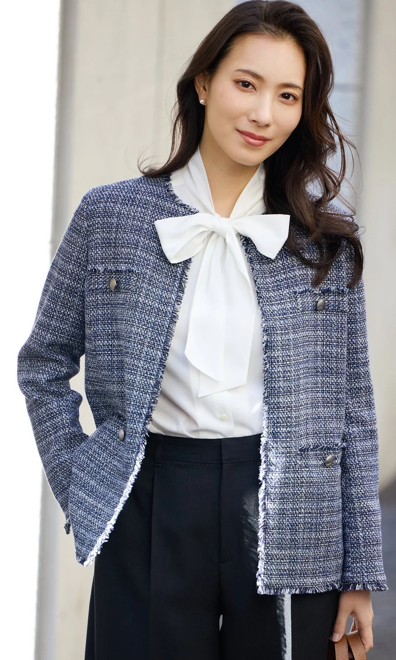 ネイビーのツイードジャケットと白いボウタイブラウスを着用した女性