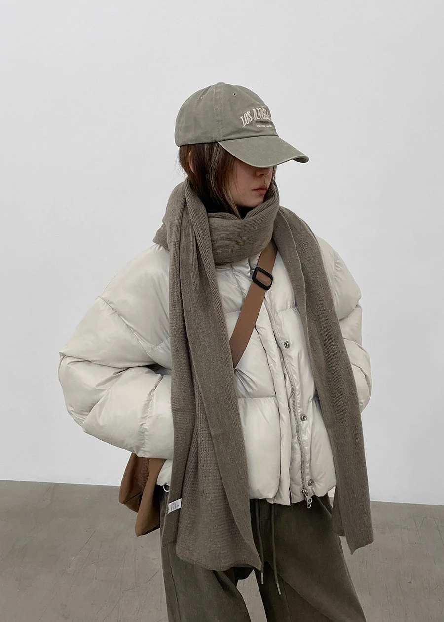 白いダウンジャケットにグレーのマフラーとキャップを合わせた、カジュアルで暖かそうな冬のコーディネートの人物が写っています。