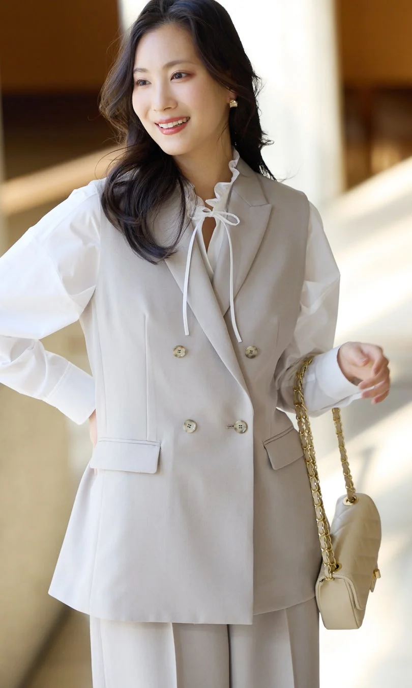 白いフリルブラウスにベージュのダブルブレストベストを着用した女性