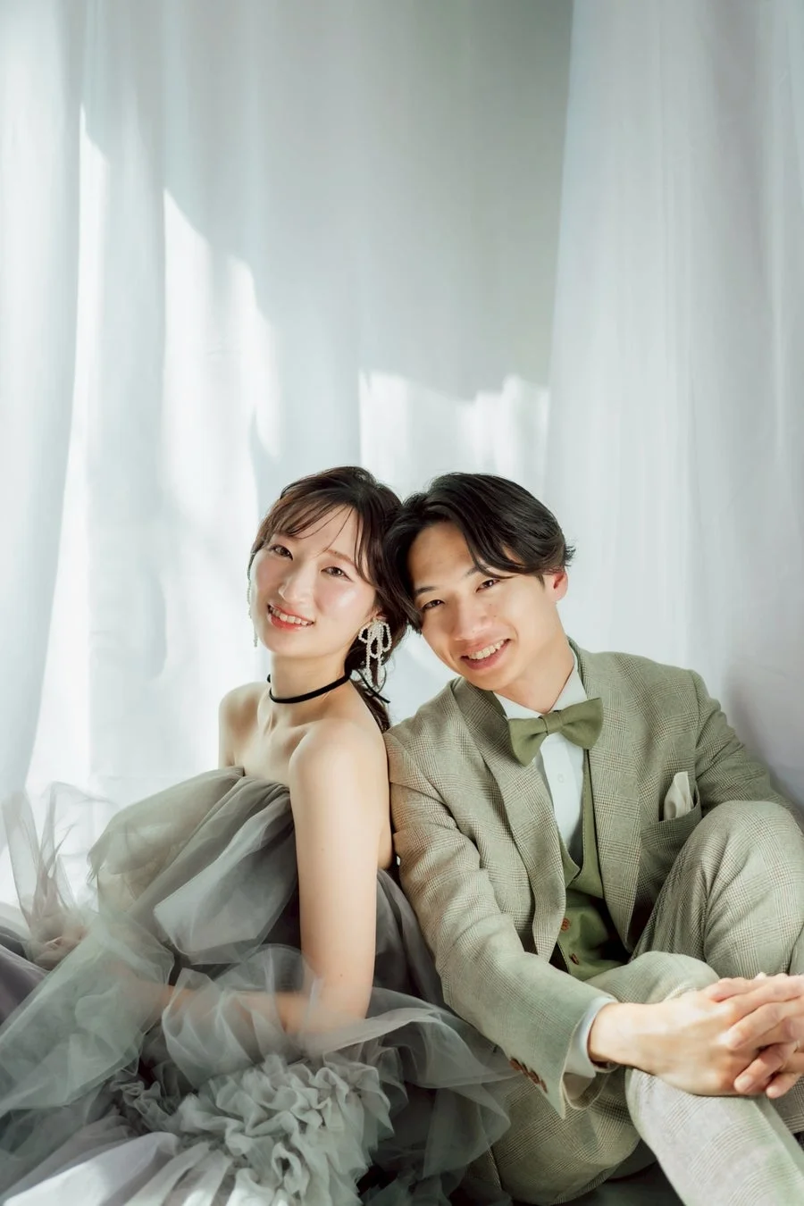 笑顔の若いカップルが背中合わせに座り、お互いに寄り添っているポートレート写真です。